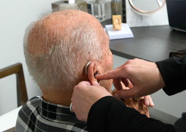 An older man gets an adjustment made to hearing aid